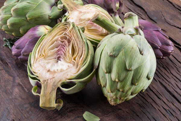 Green and purple artichoke flower edible buds on wooden background.