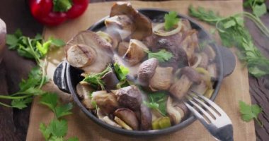 Kızarmış porcini mantarlı tava eski bir ahşap masada duruyor ve buhar yayıyor. Sabah ışığı. 