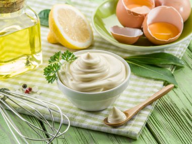 Ortasında mayonez sosu olan bir kase ve ahşap masanın etrafında mayonez malzemeleri..