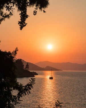 Sakin deniz ve gün batımı. Güneş ufuktaki tepelerin ardında batıyor. Güzel doğa arkaplanı.
