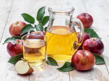 Bir bardak meyve suyu, bir sürahi taze elma suyu ve ahşap masada organik elmalar..