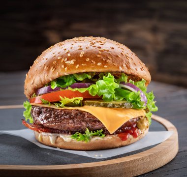 Arkası koyu kahverengi olan ahşap bir masada lezzetli bir hamburger. Fast food konsepti.