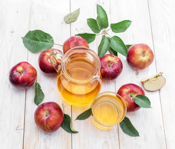 Glass of juice and carafe of fresh apple juice and organic apples on wooden table.