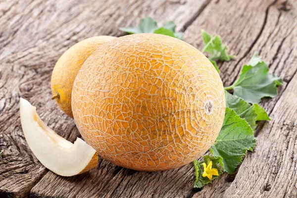 Ripe yellow melon with slices and melon leaves on a old wooden table.