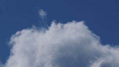 Yakın plan 4K hızlandırılmış mavi güneşli gökyüzünde beyaz büyük bulutların videosu. Yaz mavi bulutlu gökyüzü zaman atlaması. Bulutların arasında bir uçak uçurmanın etkisi.