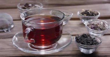 Damla yavaşça bir bardak çaya düşer. Etrafta farklı yaprak çayları olan küçük kaseler var. Klasik ahşap masa.. 