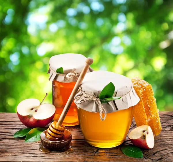 Latas de vidrio llenas de miel y manzanas en el jardín . — Foto de Stock