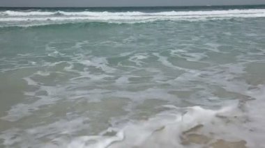 Kumlu bir sahilde okyanus dalgaları.