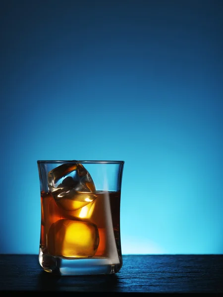 Pohár whiskyt jéggel, kék háttérrel. — Stock Fotó