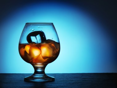 Glass of whiskey with ice on a blue background.