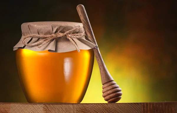 Glass can full of honey and wooden dripper on brown background. — Stock Photo, Image