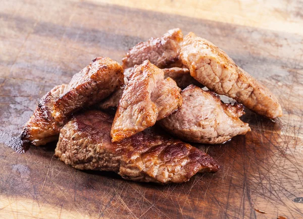 Trozos de carne asada sobre tabla de madera . — Foto de Stock