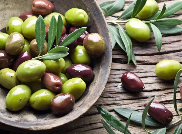 Tigela de madeira cheia de azeitonas e ramos de oliveira além dele . — Fotografia de Stock