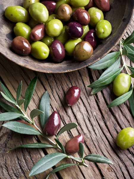 Ciotola di legno piena di olive e ramoscelli d'ulivo oltre ad esso . — Foto Stock