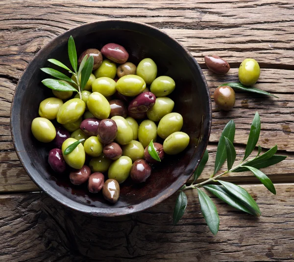 Wooden bowl full of olives and olive twigs besides it. — Free Stock Photo