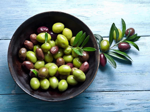 Holzschale voller Oliven und Olivenzweige daneben. — Stockfoto
