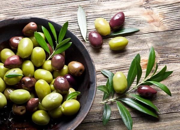 Ciotola di legno piena di olive e ramoscelli d'ulivo oltre ad esso . — Foto Stock