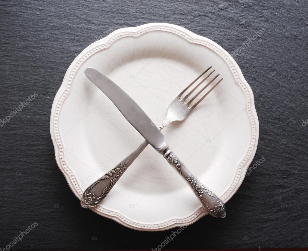 Silver cutlery  and vintage plate on a dark grey background.