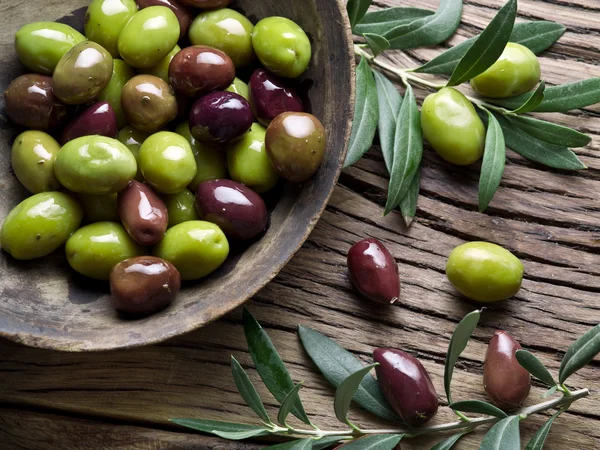 Cuenco de madera lleno de aceitunas y ramitas de olivo a su lado . — Foto de Stock