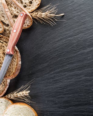 Ekmek dilimleri, bir buğday ve siyah taş masa üzerinde bir bıçak.