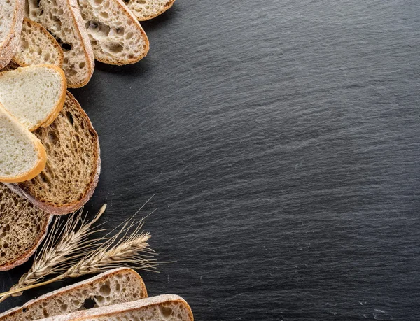 Bread slices, a wheat and a knife on the black stone desk. — Stock Photo, Image