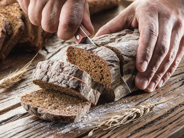 Man's handen snijden brood op de houten plank. — Stockfoto