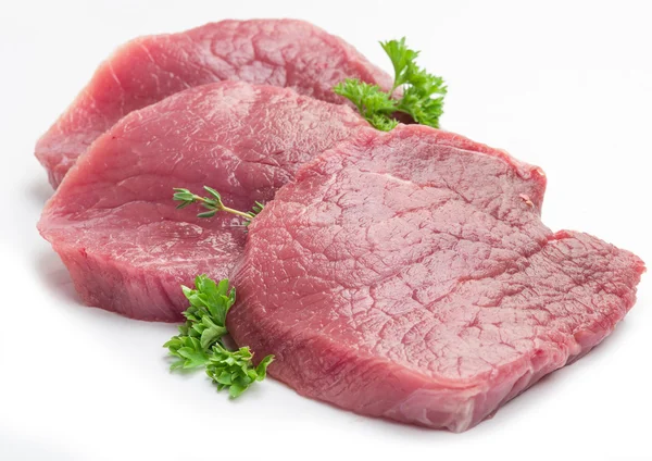 Rå nötkött biffar med persilja på vit bakgrund. — Stockfoto