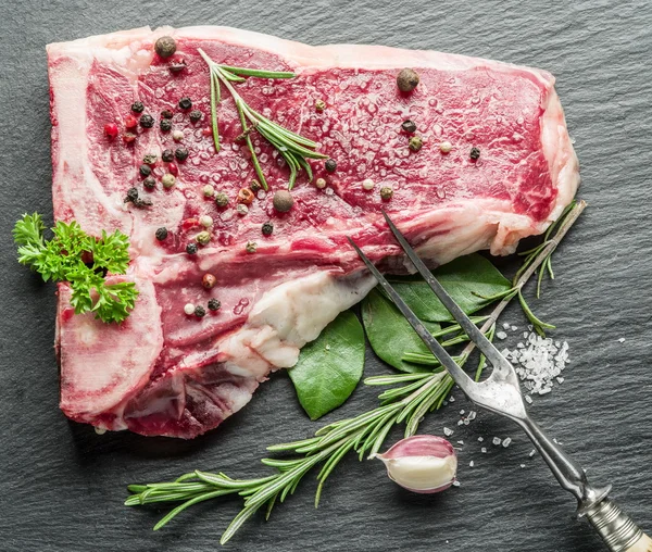 Bife cru com especiarias na tábua de corte preta . — Fotografia de Stock