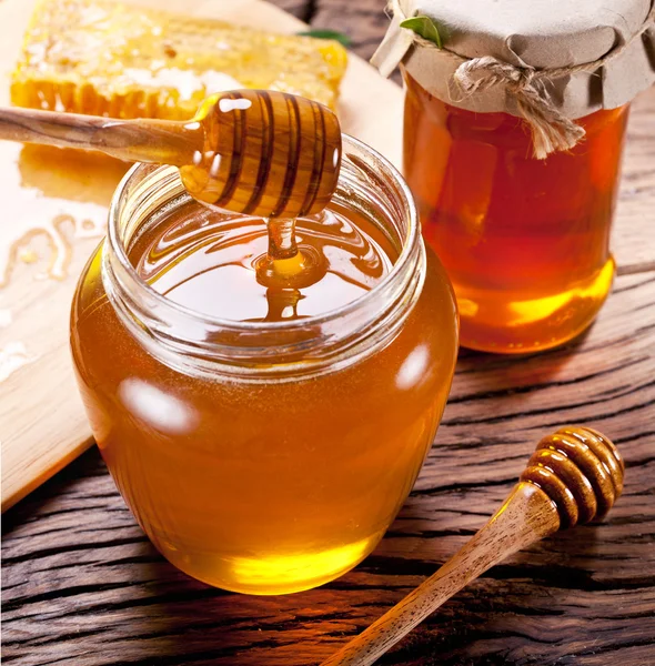 Honey dripping from wooden spoon into glass can. — Stock Photo, Image