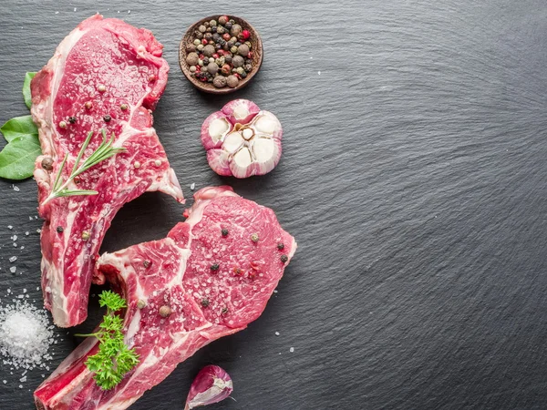 Rohe Beaf-Steaks mit Gewürzen auf schwarzem Schneidebrett. — Stockfoto