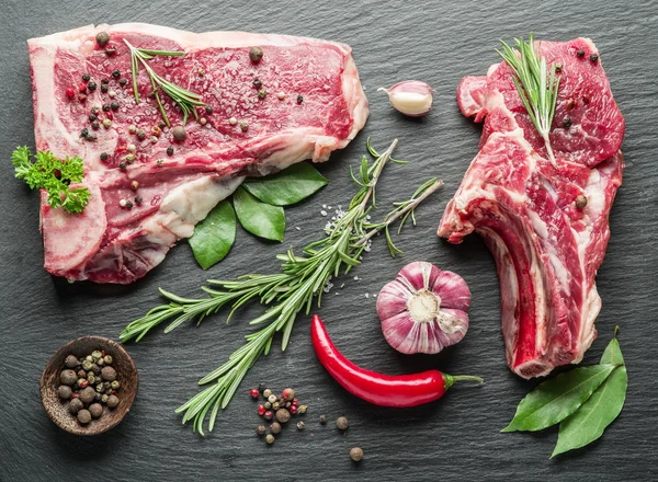 Bifes crus com especiarias na tábua de corte preta . — Fotografia de Stock