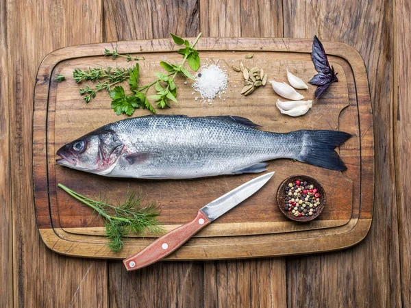 Seabass en un tablero de madera con especias y hierbas . — Foto de Stock