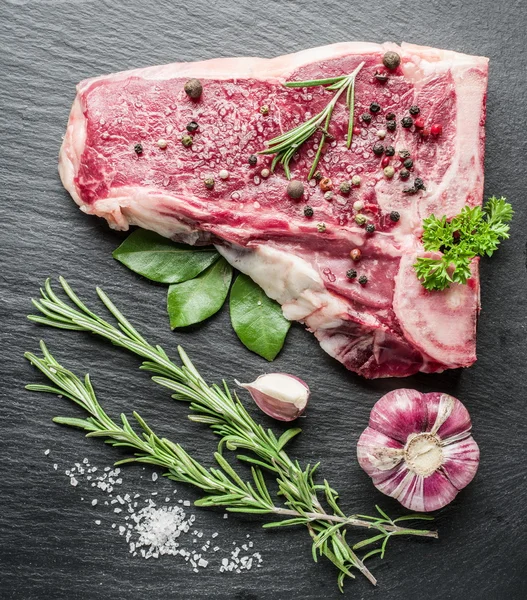 Ruwe rundvlees steaks met specerijen op de zwarte snijplank. — Stockfoto