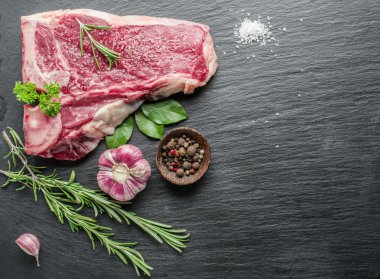 Ham sığır eti biftek siyah kesme tahtası üzerinde baharatlar ile.