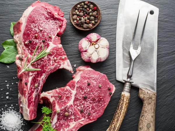 Raw beaf steaks with spices on black cutting board. — Stock Photo, Image