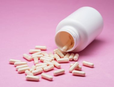 Beyaz kapsüller ya da tabletler pembe arka planda plastik şişeden dökülüyordu. İlaç, sağlık, gıda takviyesi ve ilaç tedavisi kavramı.