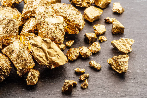 Золотые самородки на фоне черного камня вид сверху. Имитация золотых самородков.