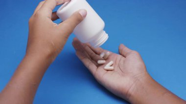 Beyaz kapsüller ya da plastik şişeden mavi arka plana dökülen haplar. İlaç, sağlık, takviye ve ilaç tedavisi kavramı.