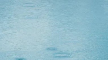 Havuzun pürüzsüz yüzeyine yağmur damlaları düşüyor. Yavaş çekim orta çekim görünümü.