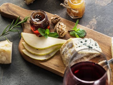 Kırsal ahşap tahtada çeşitli peynir tabakları ve bir bardak kırmızı şarap. Şarap tatmak için çeşitli sert ve yumuşak peynirler. Restoran menüsü kavramı.