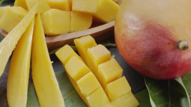 Olgun mango meyveleri, dilimler ve mango yapraklarıyla gri taş bir masanın üzerinde yavaşça hareket eder. Projelerin için güzel bir meyve arka planı. Makro video çekimi.