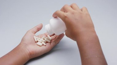 Beyaz kapsüller ya da plastik şişeden açık gri arka plana dökülen haplar. İlaç, sağlık, takviye ve ilaç tedavisi kavramı.