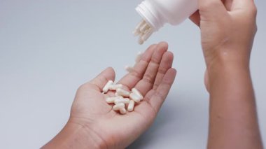 Beyaz kapsüller ya da plastik şişeden açık gri arka plana dökülen haplar. İlaç, sağlık, takviye ve ilaç tedavisi kavramı.