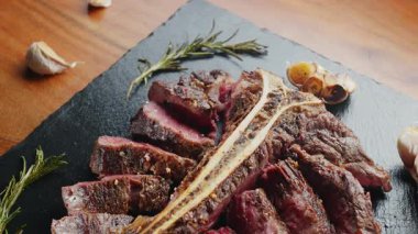 Orta pişmiş T-Bone bifteği, otlar ve sarımsaklı servis panosuna yakın çekim. Üst görünüm.