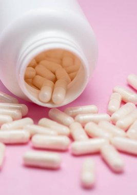 Beyaz kapsüller ya da tabletler pembe arka planda plastik şişeden dökülüyordu. İlaç, sağlık, gıda takviyesi ve ilaç tedavisi kavramı.