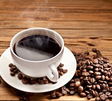 Bir fincan sıcak, sade kahve ve ahşap masanın üzerinde kavrulmuş kahve çekirdekleri..