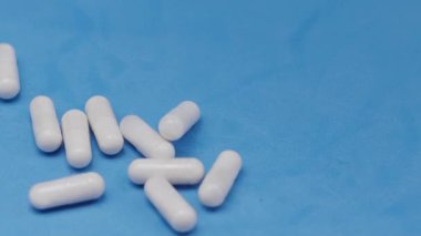 Yavaş çekim videosu: mavi arka plana düşen beyaz haplar ya da kapsüller. İlaç, sağlık, takviye ve ilaç tedavisi kavramı.