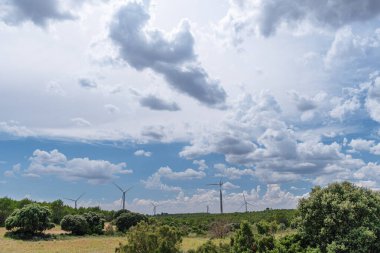 Kırsal alanda rüzgar türbinleri ve arka planda çarpıcı bulutlu gökyüzü. Çevre dostu elektrik enerjisi üretimi.