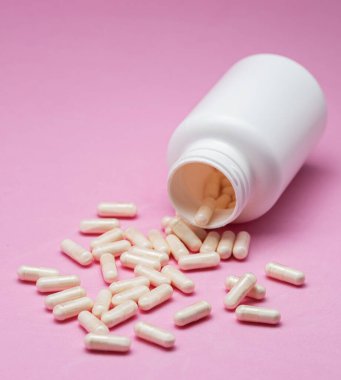Beyaz kapsüller ya da tabletler pembe arka planda plastik şişeden dökülüyordu. İlaç, sağlık, gıda takviyesi ve ilaç tedavisi kavramı.