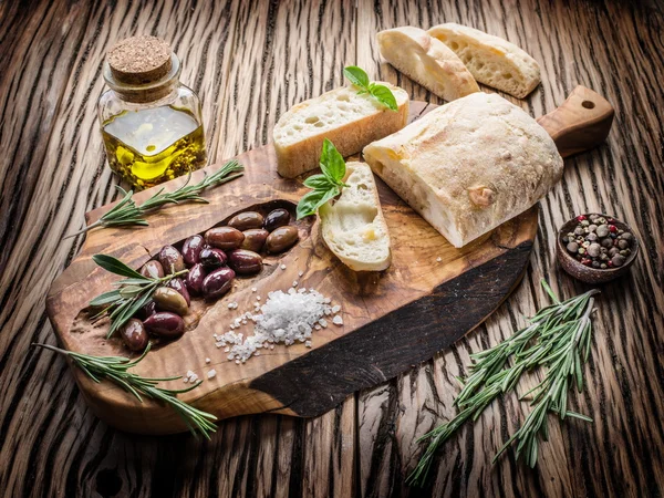 Ciabatta, olivy a nivou na dřevo. — Stock fotografie